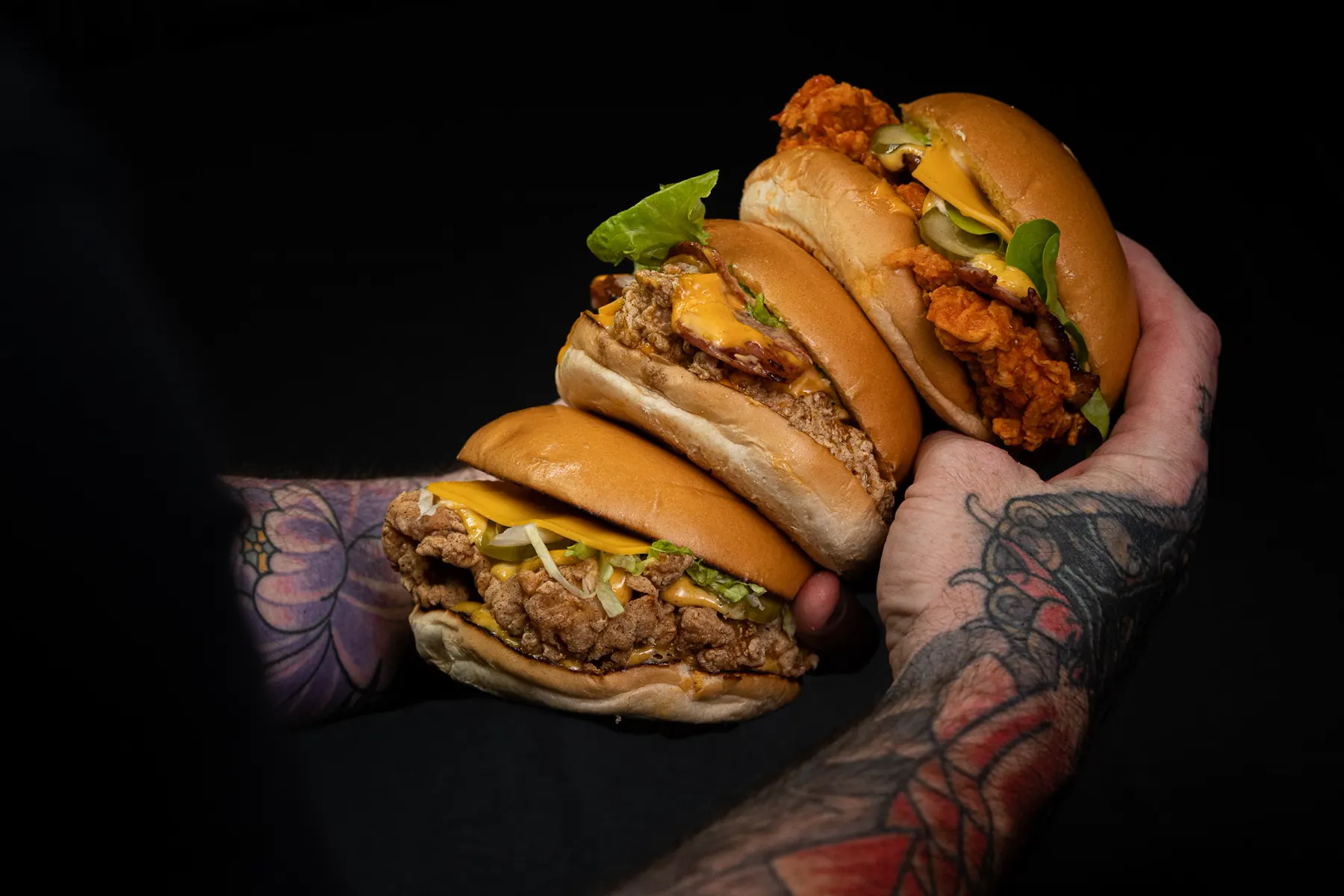 Three fried chicken burgers from Mr Jeebus, held up against a black background.
